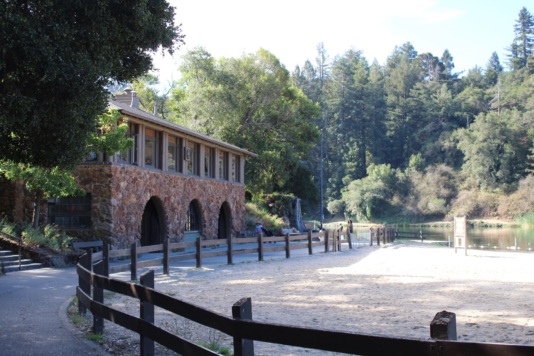 A weathered wooden boathouse standing at the edge of still water beneath tall trees